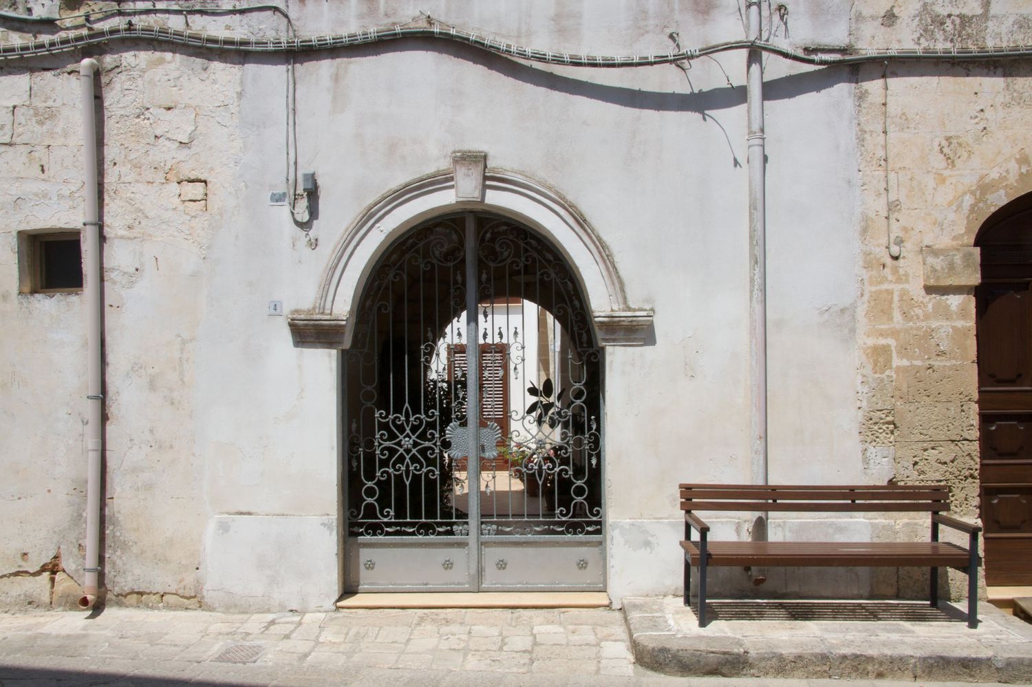 Ornate wrought iron gate set in a stone archway with a wooden bench beside it.