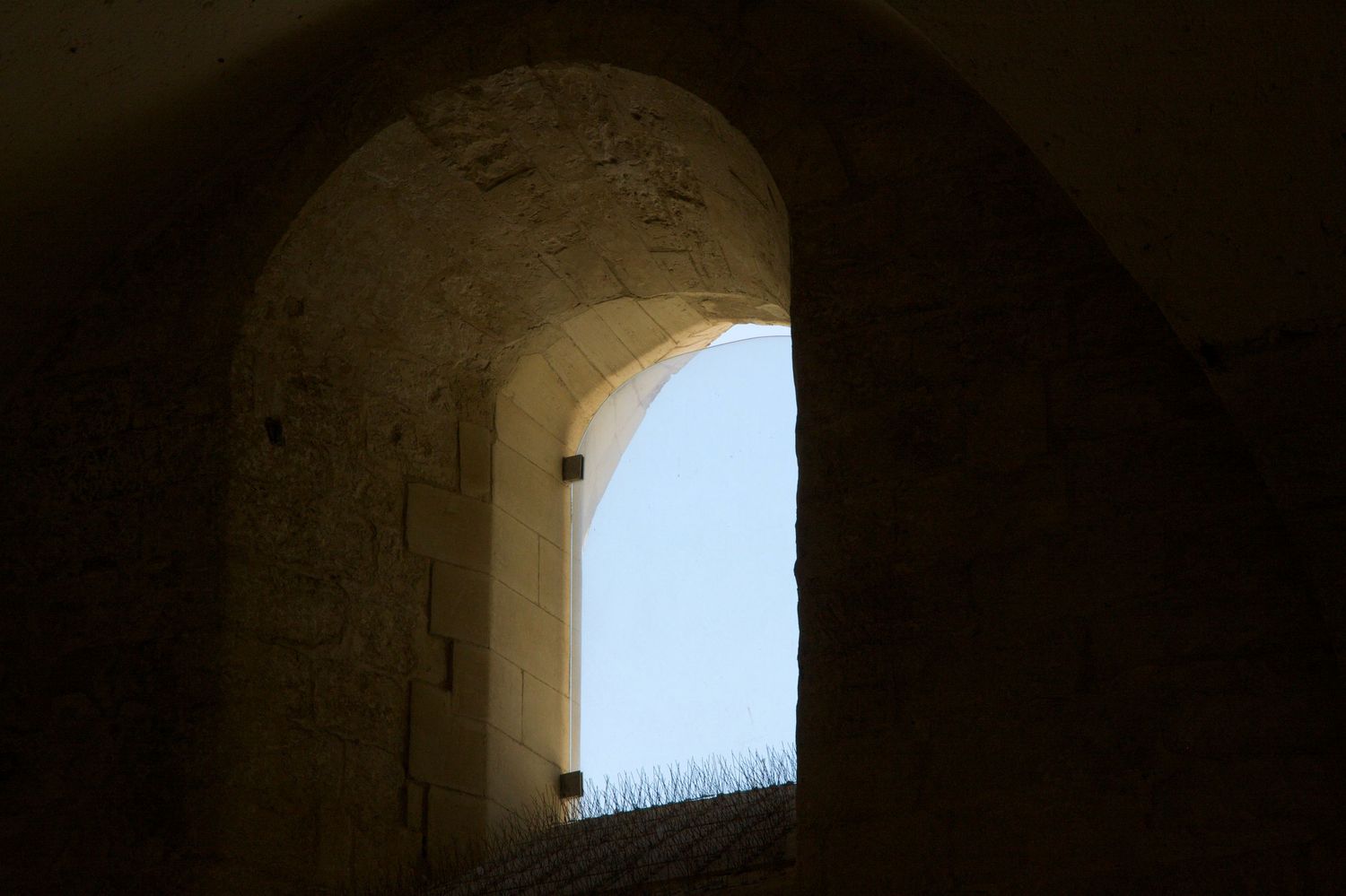 Stone arched window tunnel opening to bright blue sky in an ancient fortress or castle wall.