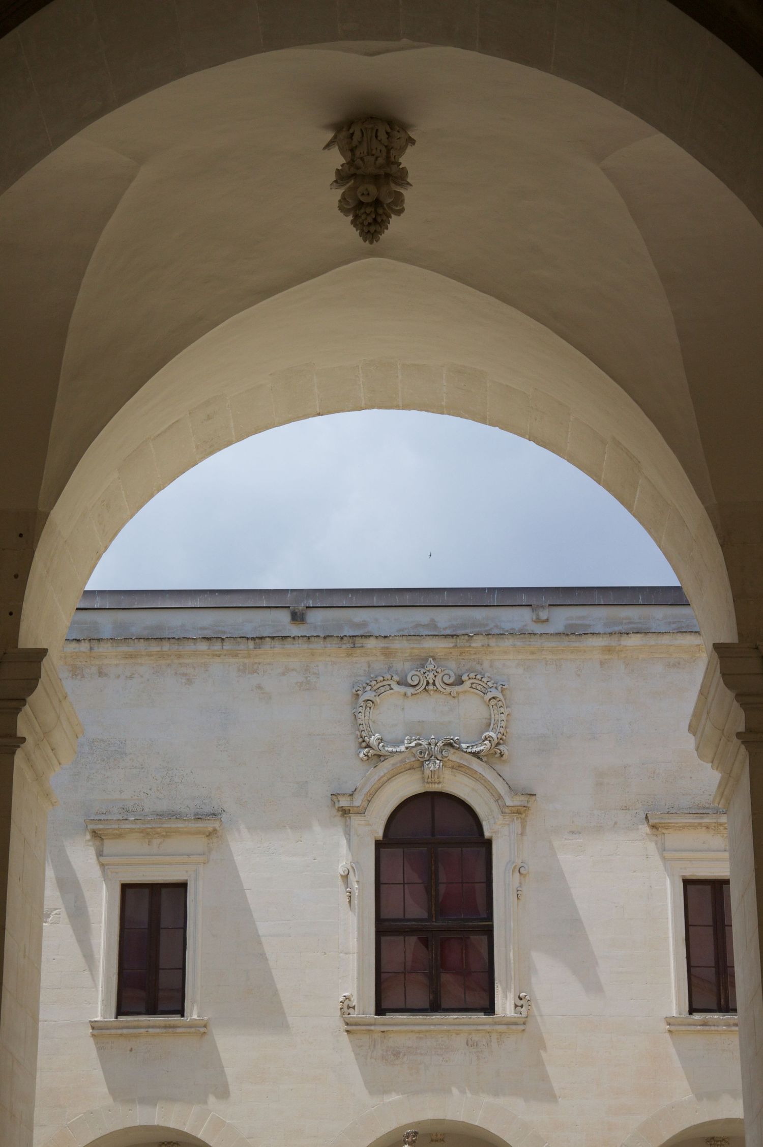 Ornate Baroque arch framing a decorative window with carved stone relief on a historic Italian palace facade.