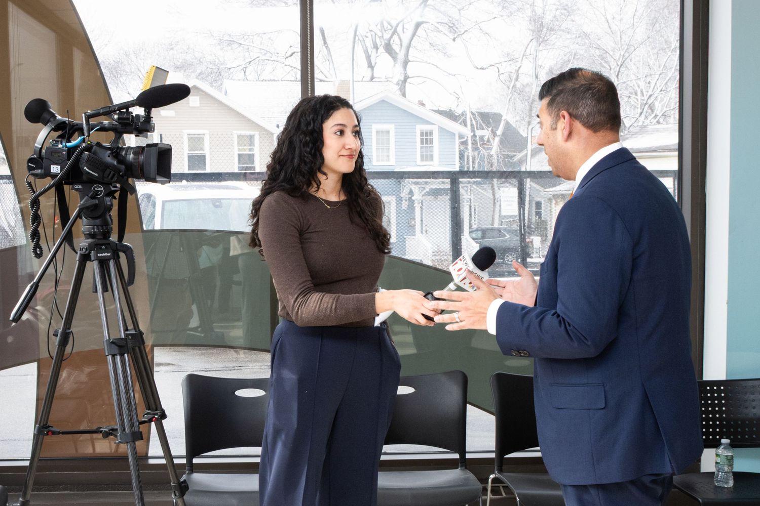 Woman being interviewed on camera by a man in a suit in a modern office setting.