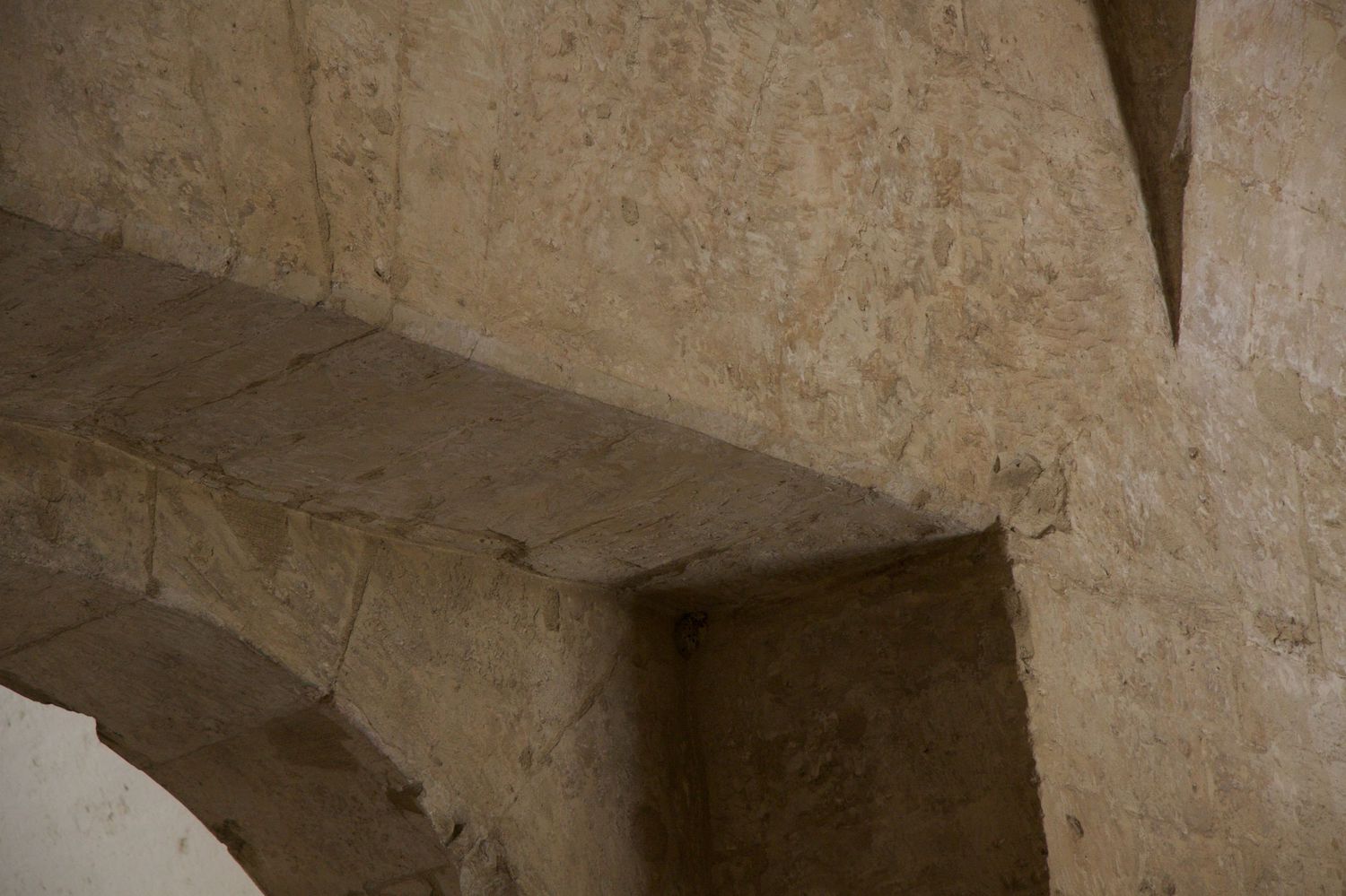 Detail of ancient limestone stone arch construction showing rough-cut blocks and angular corbel in historic building interior.