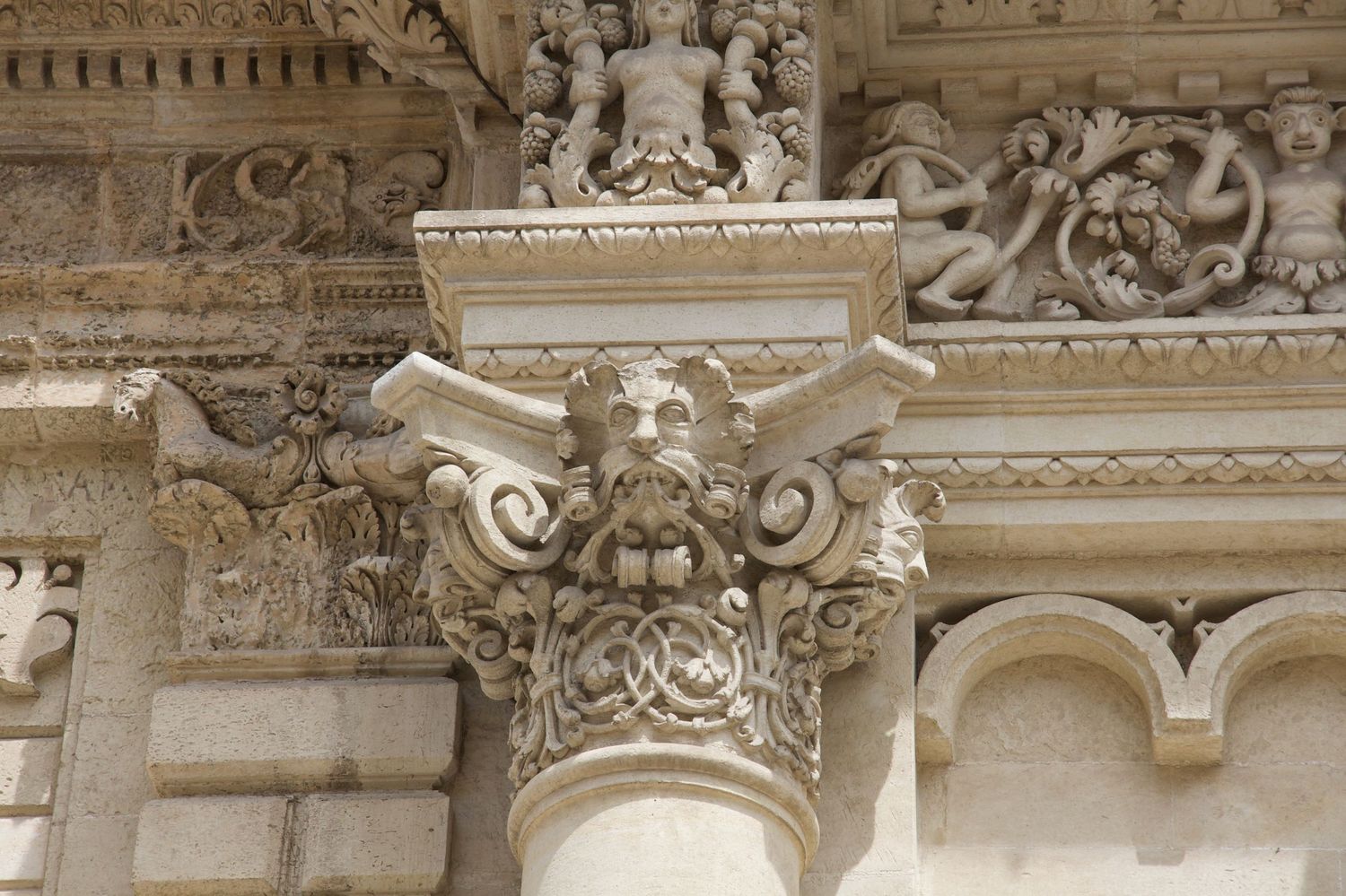 Elaborate Corinthian column capital with intricate carvings and figures on a classical stone facade.