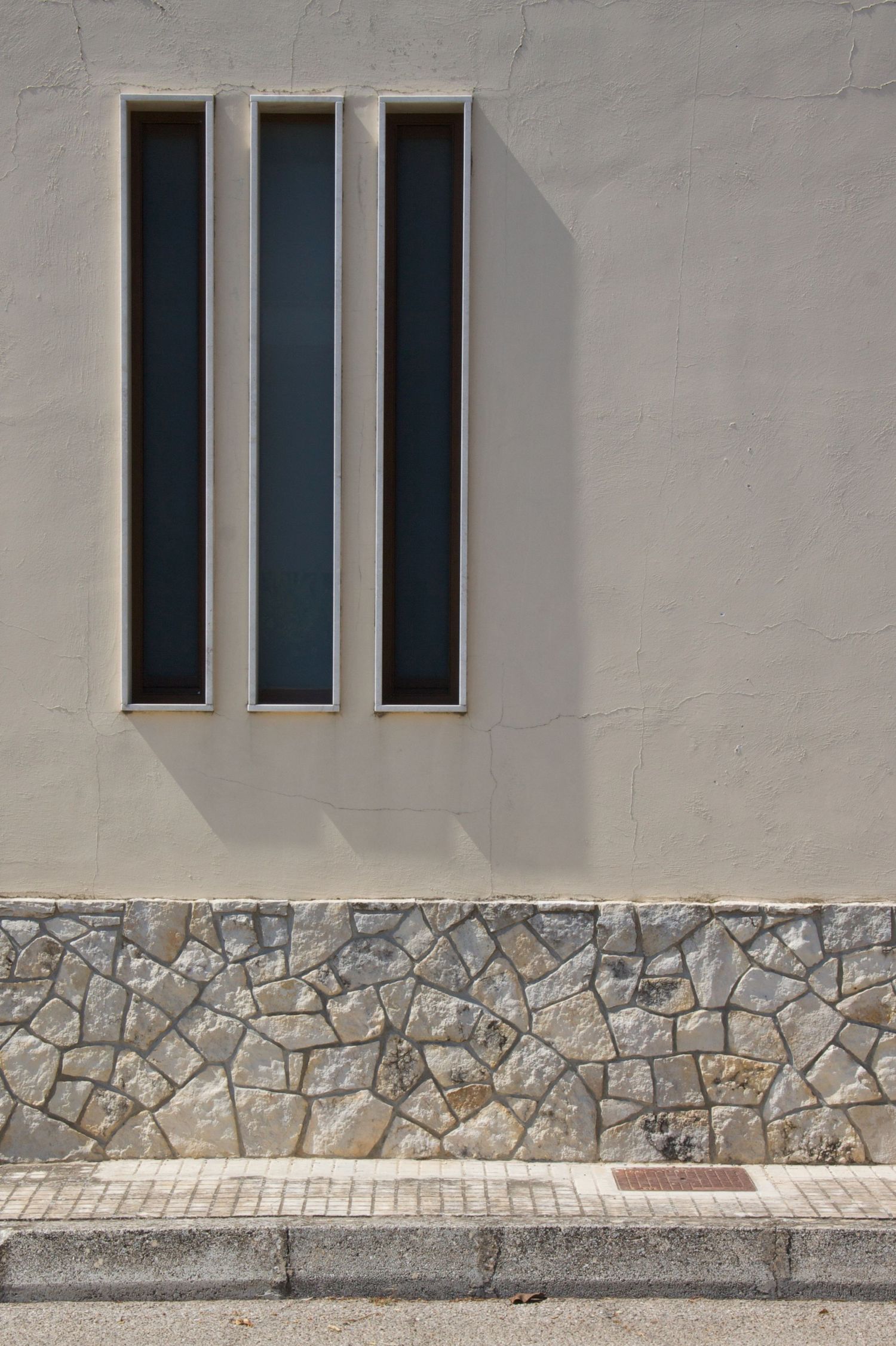 Modern building facade with three tall narrow vertical windows above a rustic stone wall base.