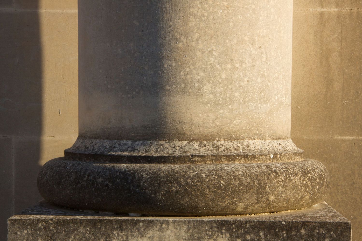 Close-up of a classical stone column base with a torus molding resting on a square plinth in warm sunlight.