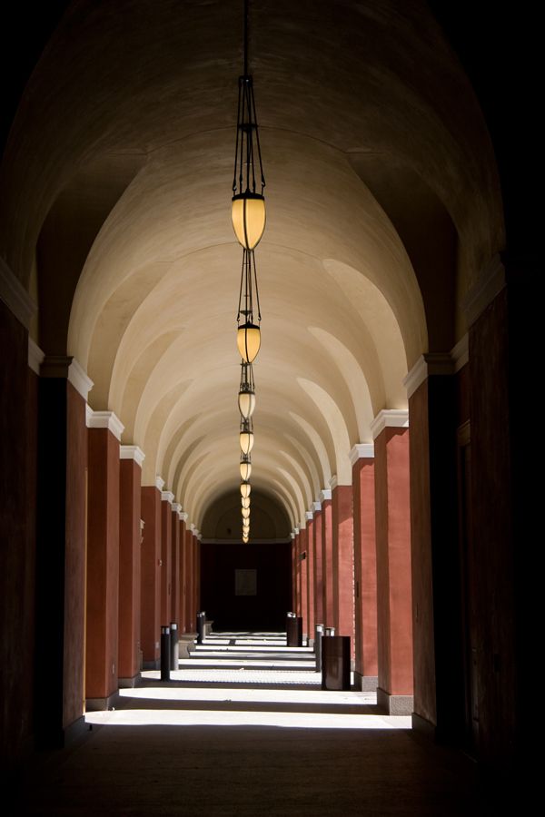Dramatic arched corridor with hanging pendant lights and terracotta columns in perspective.