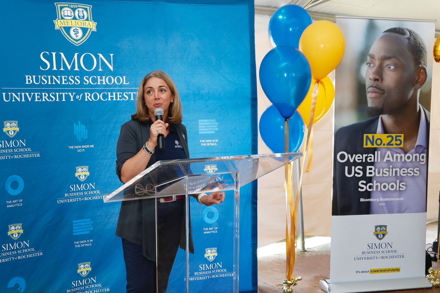 Woman speaks at Simon Business School University of Rochester podium with balloons.