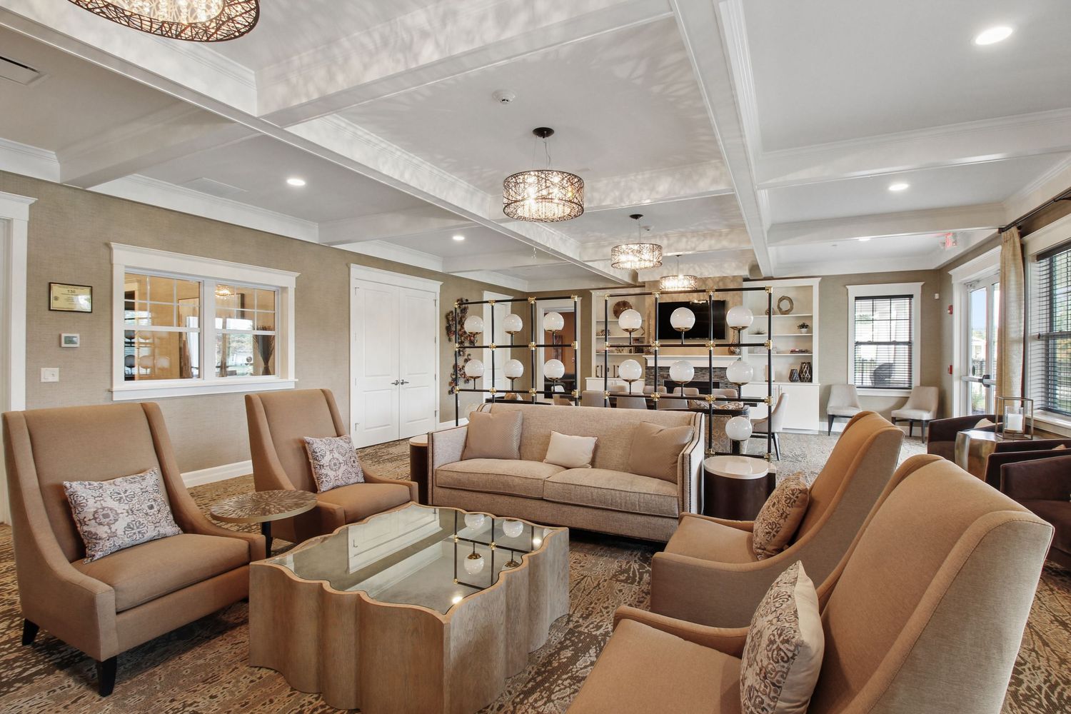 Upscale living room with coffered ceiling, beige sofas, glass coffee table, and warm lighting.