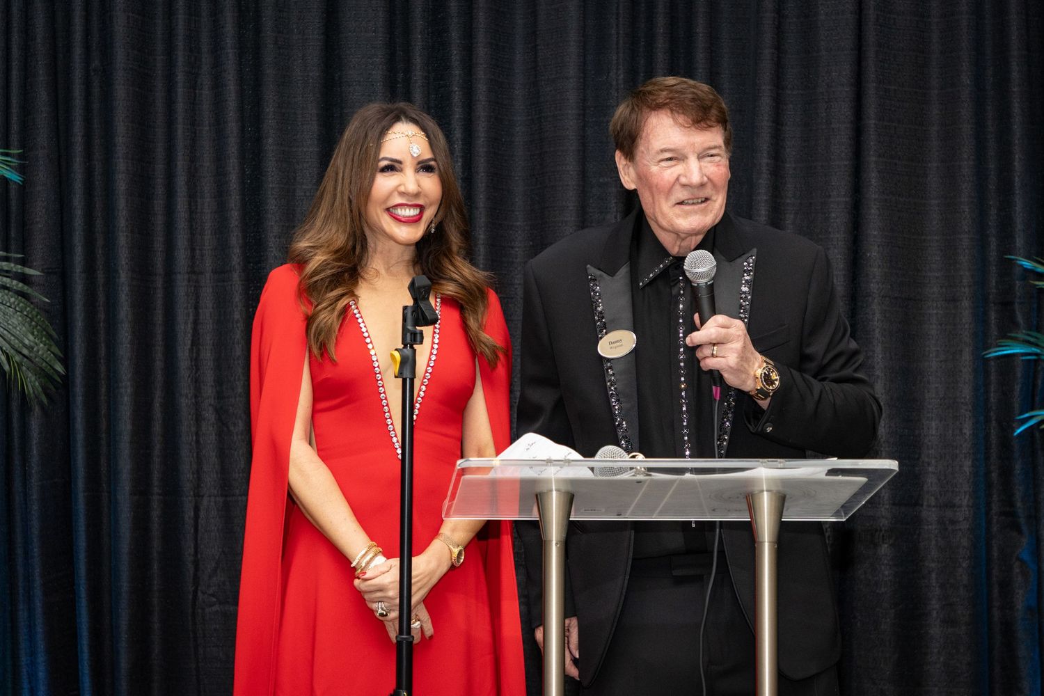Man and woman in formal attire speaking at a podium during a gala event.