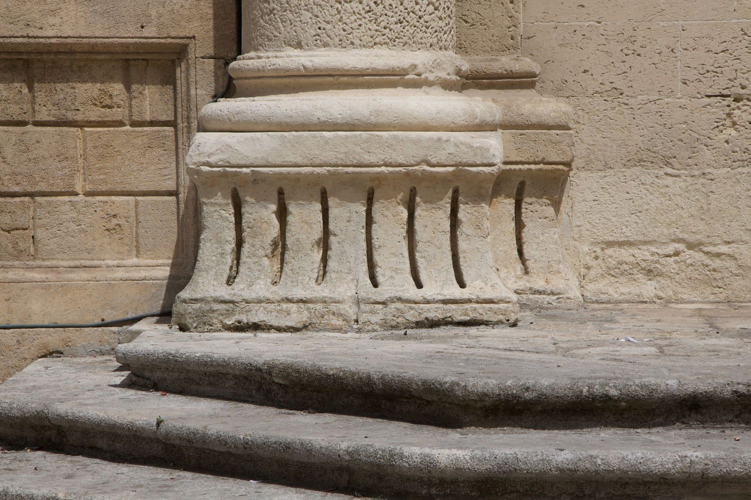 Weathered stone column base with vertical fluted grooves on worn stone steps of an old building.