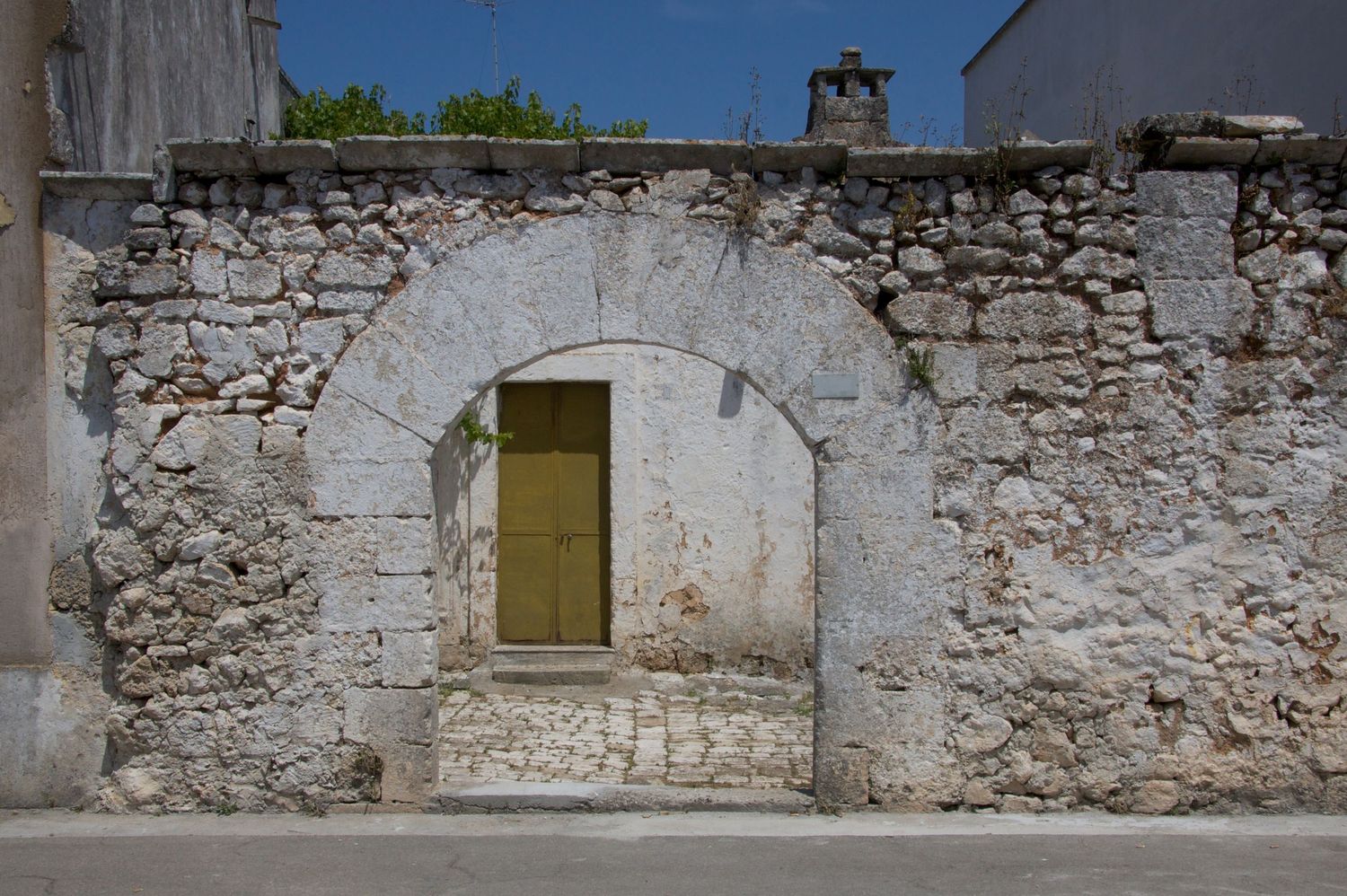 Rustic stone wall with weathered arched doorway and yellow wooden door in historic village.