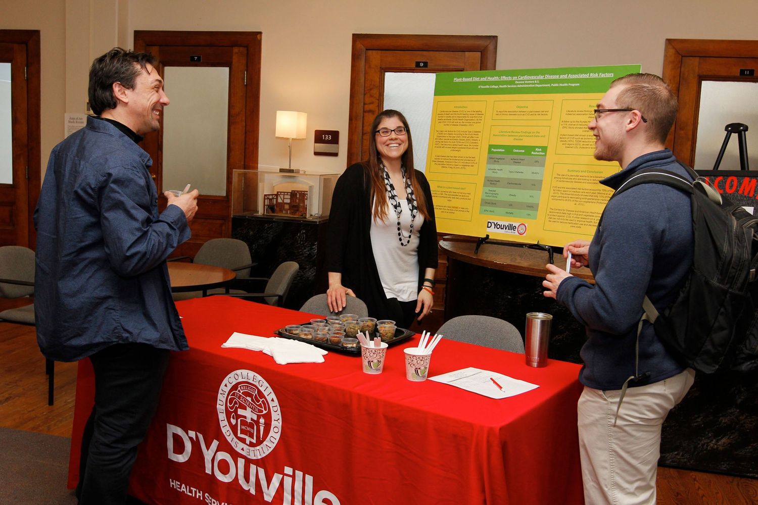 Students and professor discussing research poster at D'Youville University event.