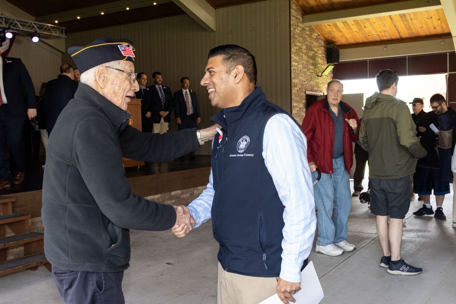Man in uniform shaking hands with another man at an outdoor community event.