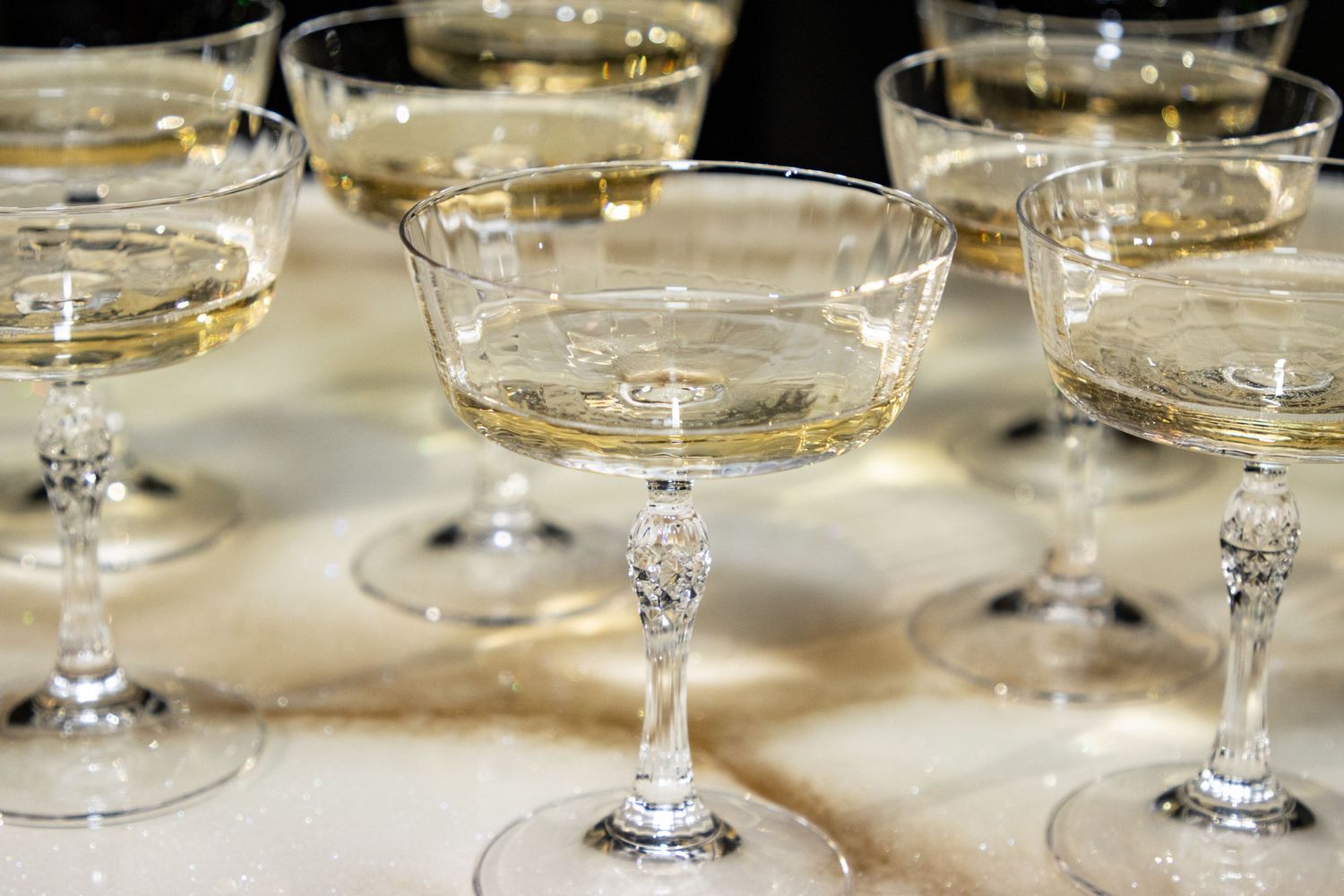 Elegant vintage crystal champagne coupe glasses filled with sparkling wine on marble surface.