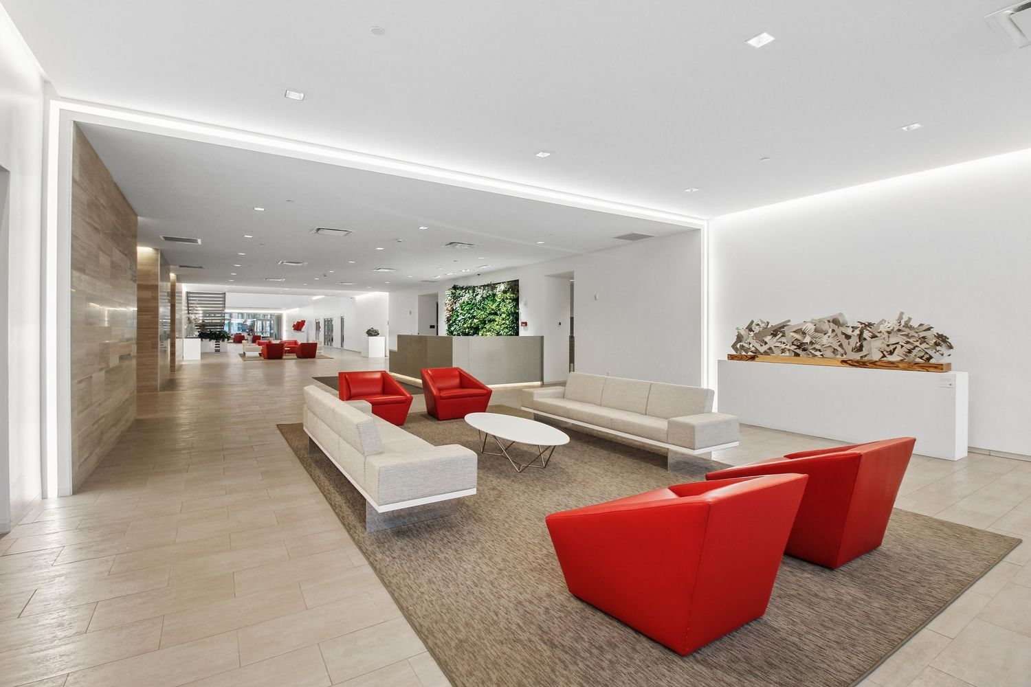 Expansive residential building lobby with red accent chairs, neutral sofas, and decorative wall art in white interiors.