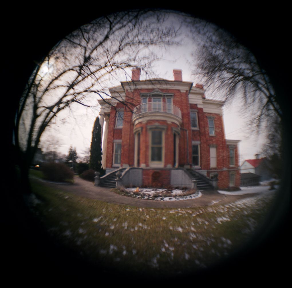 Fisheye lens view of a historic red brick Victorian mansion with arched windows surrounded by bare trees in winter.