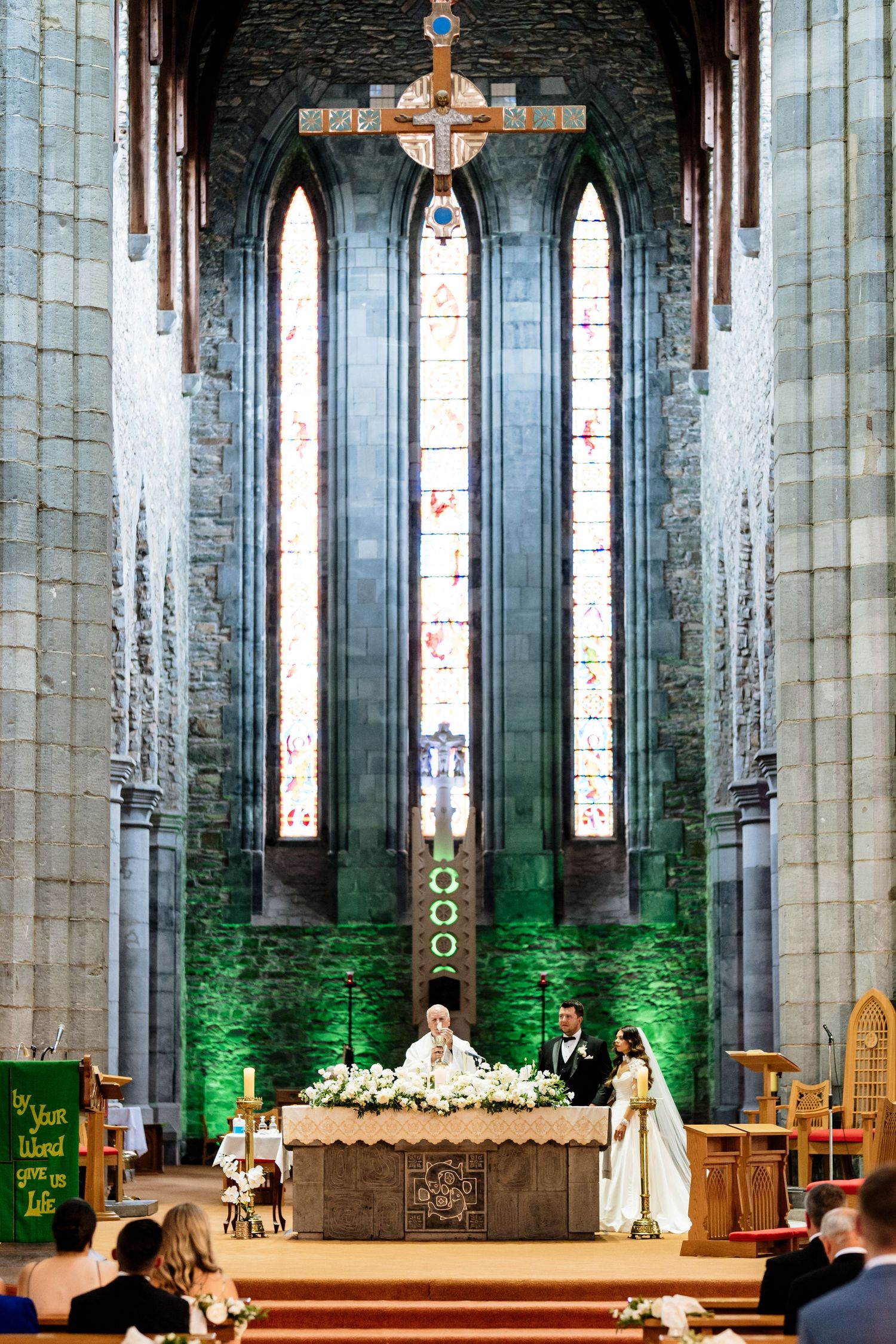 Religious ceremony taking place in a grand cathedral interior with stone columns and stained glass windows.
