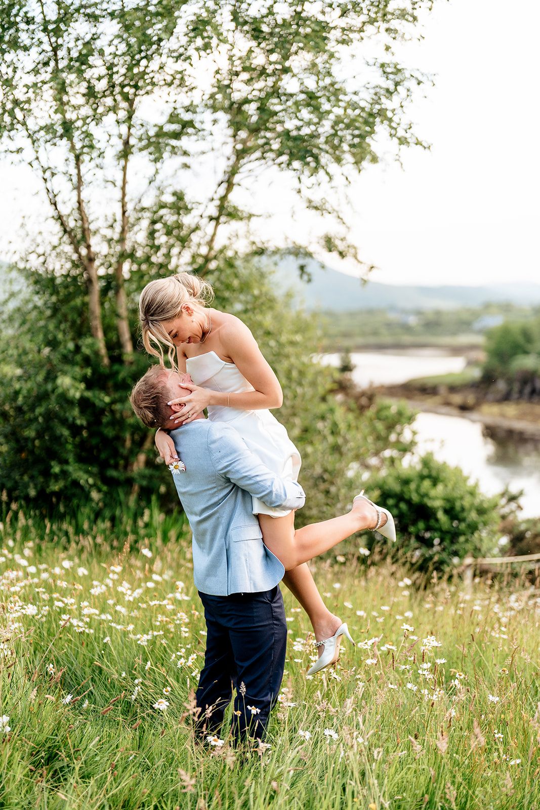 Two people share a romantic moment in a wildflower meadow overlooking a river on a sunny summer day.
