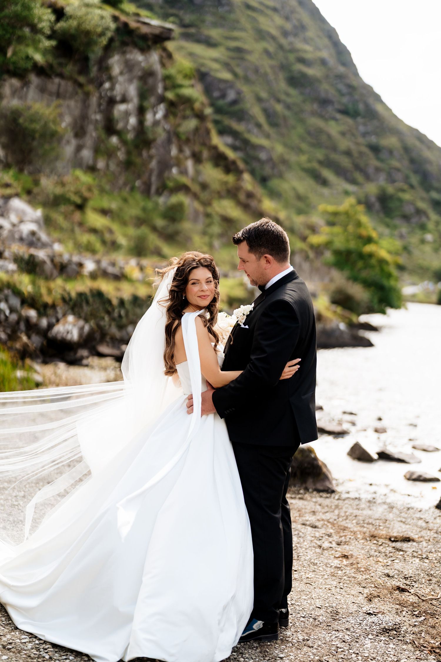 Wedding couple dances romantically on scenic coastal beach with dramatic cliffs in the background.