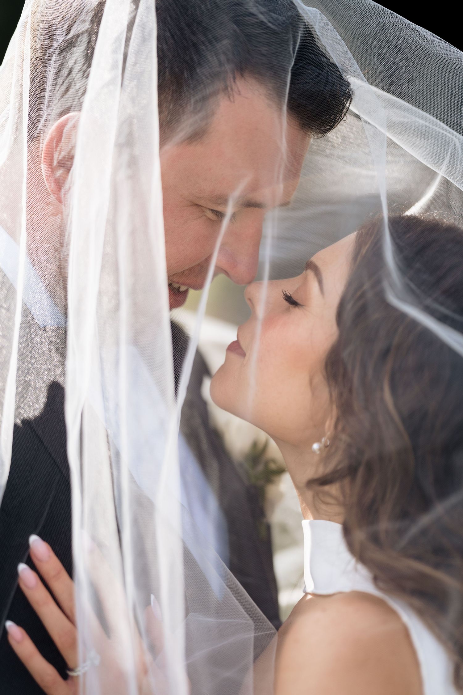 Romantic wedding couple sharing an intimate kiss under a delicate white veil on their special day.