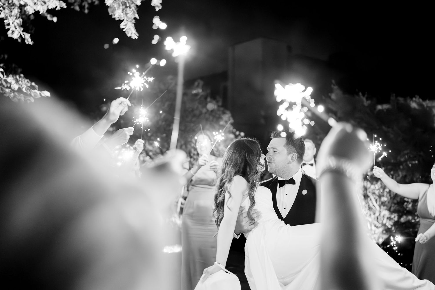 A romantic black and white wedding celebration scene under twinkling lights at night.