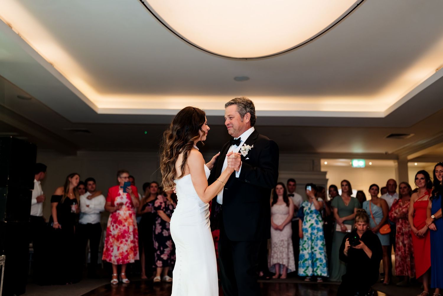 Wedding guests dance together on a dimly lit dance floor during a lively reception celebration.
