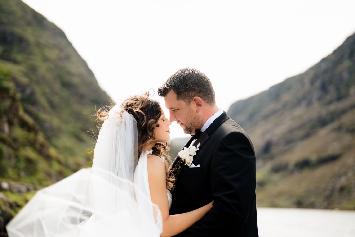 A couple in wedding attire shares an intimate moment against a backdrop of dramatic mountain scenery.