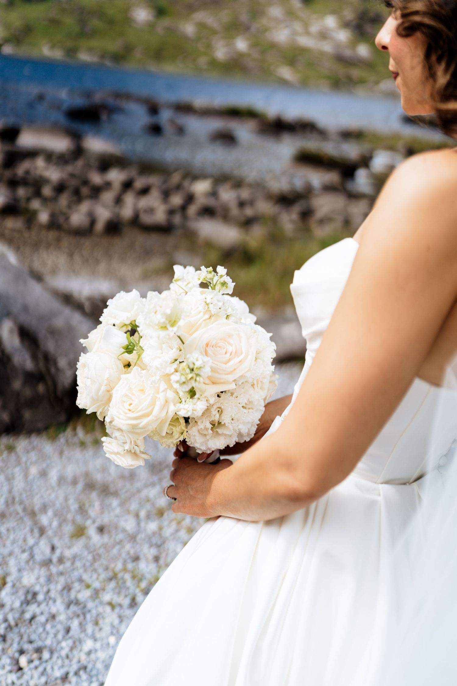 A delicate white bridal bouquet featuring pale roses and flowers is held against a white wedding dress.