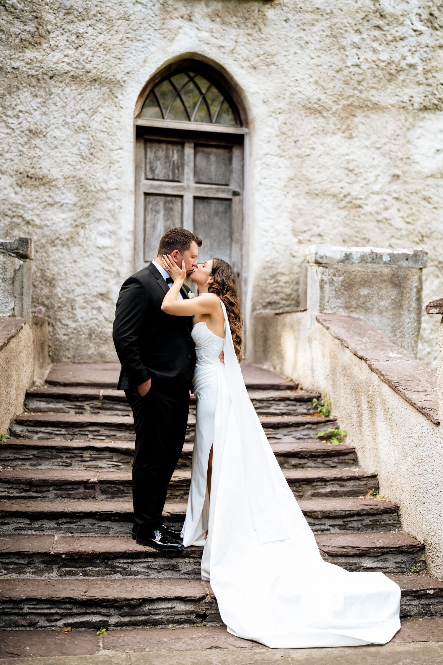 Romantic wedding moment captured on stone steps outside historic church door with elegant white flowing gown.