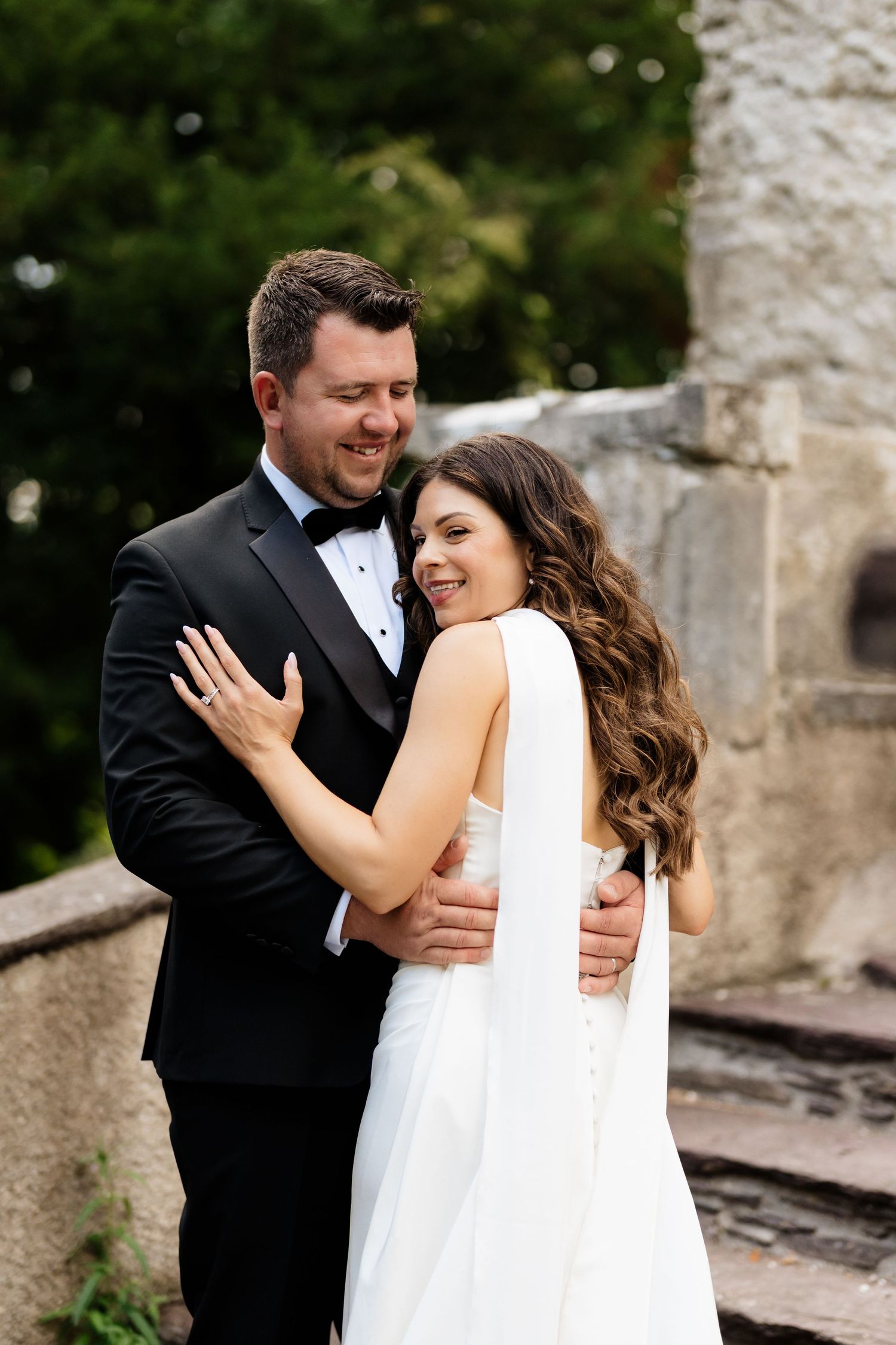 A romantic wedding moment with a couple embracing against a stone wall backdrop in formal attire.