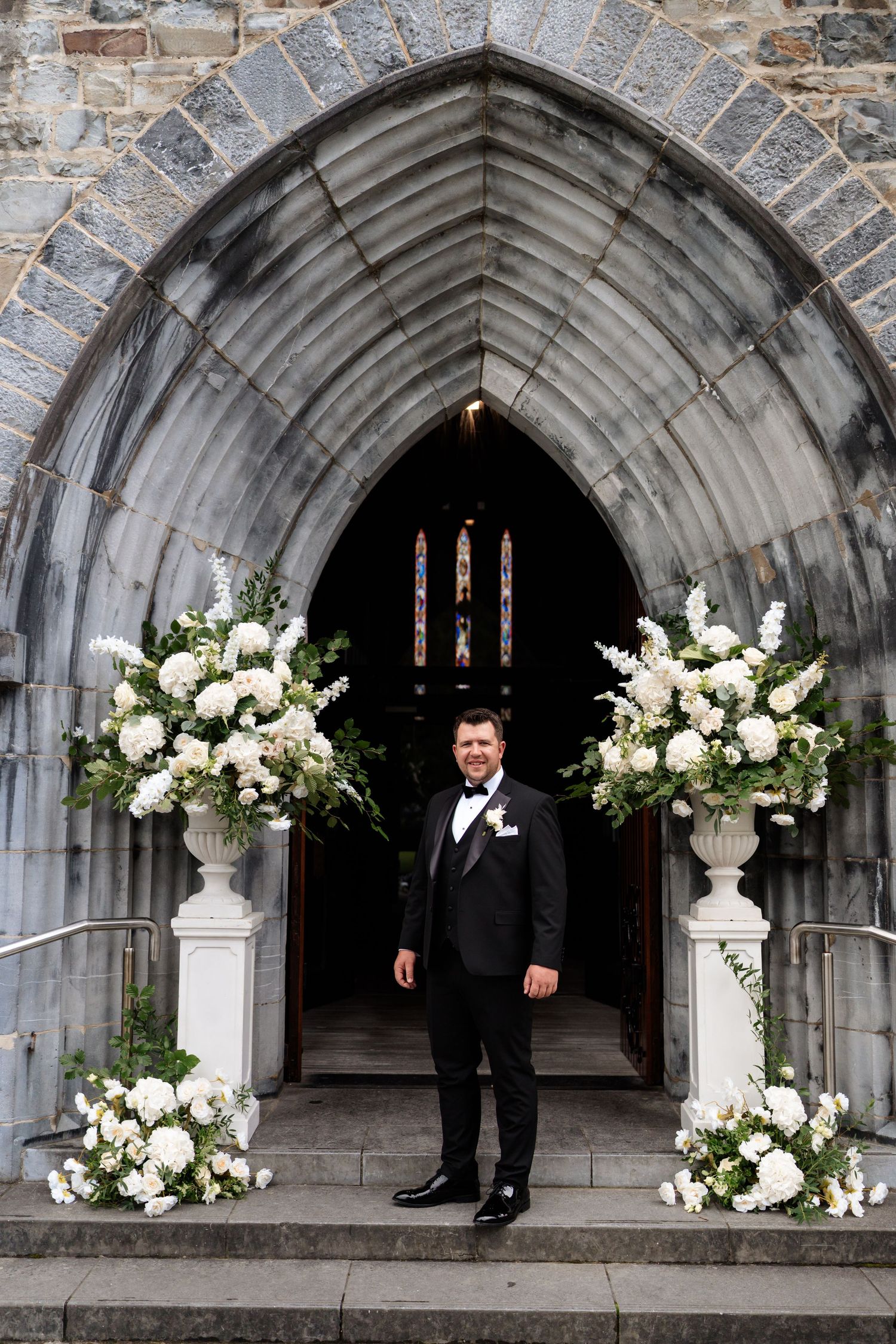 Four wedding photos show stone archways decorated with elegant white floral arrangements at church entrance.