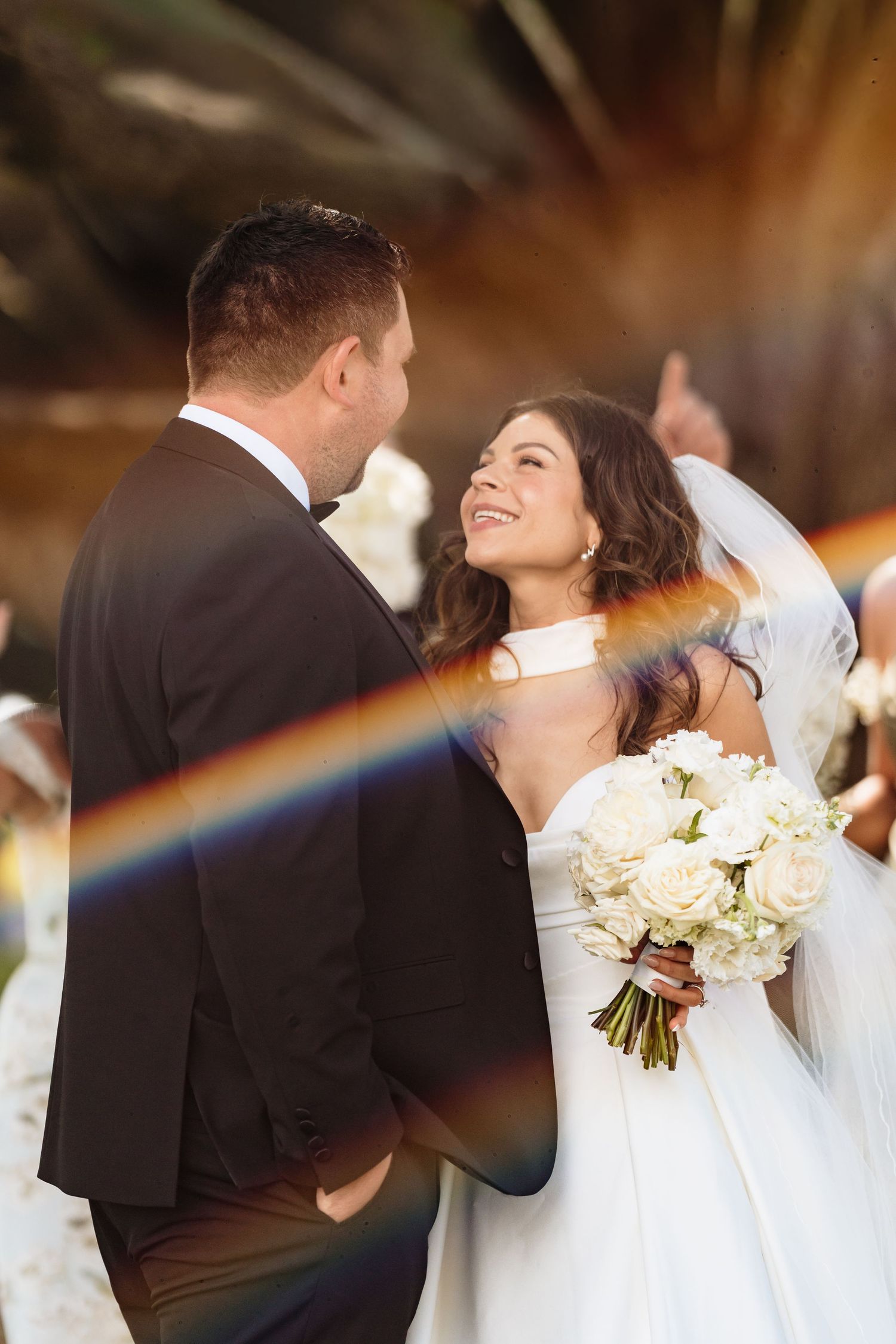 Rainbow prism light effect overlays wedding couple portrait series with white roses and formal attire.