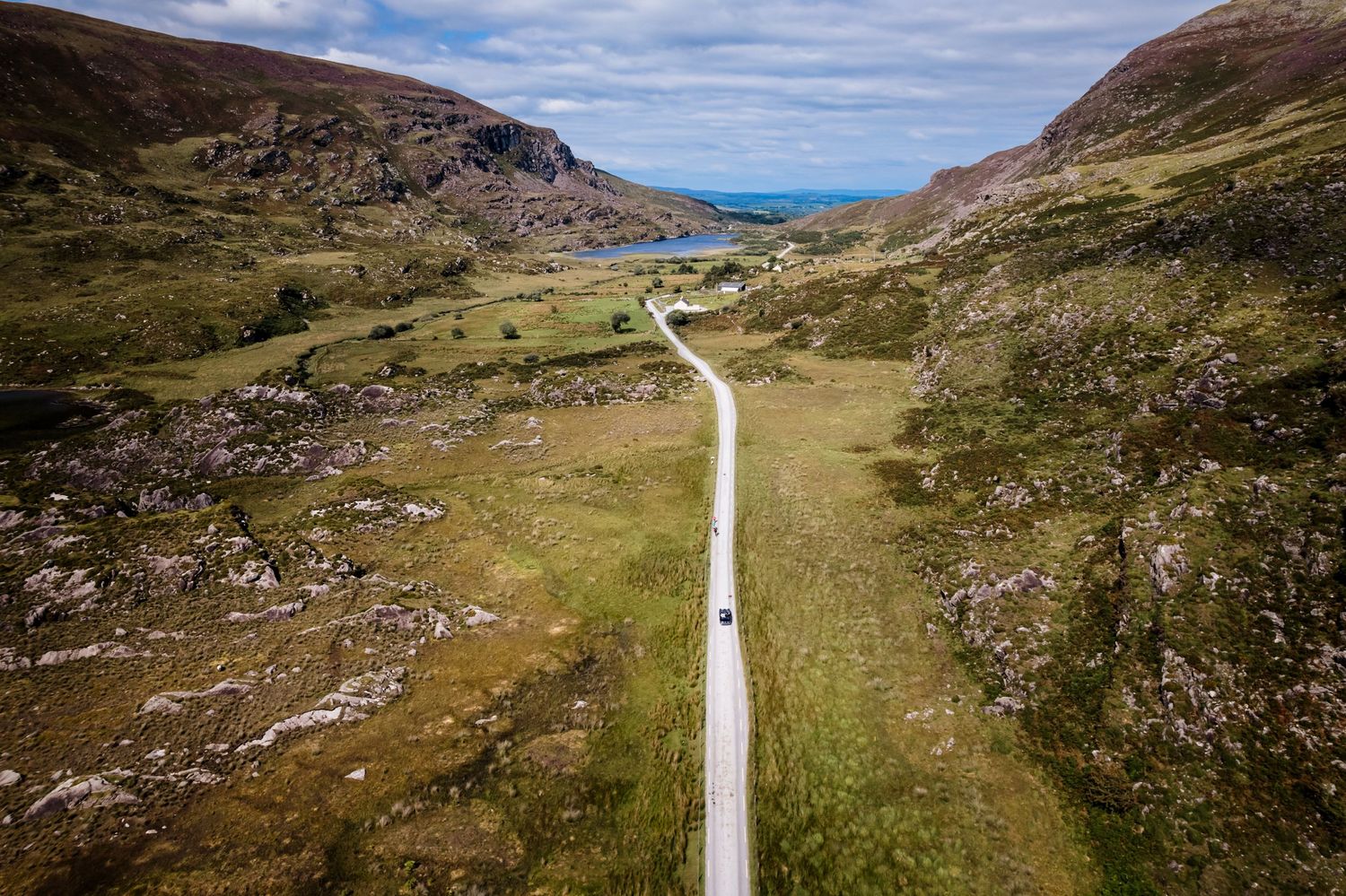 A scenic winding road curves through the rugged Scottish Highland landscape with mountains and coastal views in the distance.