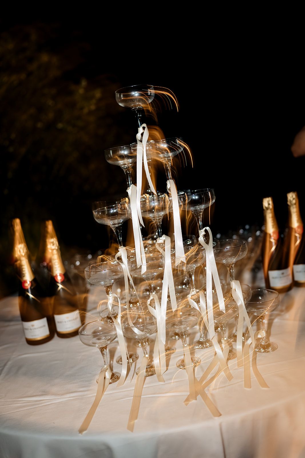 Wine glasses and empty champagne bottles lined up on a white table with candlesticks for an elegant event setting.