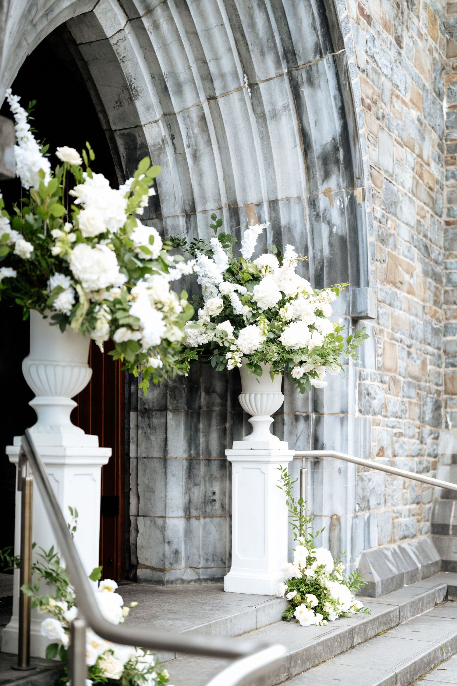 White floral arrangements in classic urns line a stone archway in an elegant church corridor.