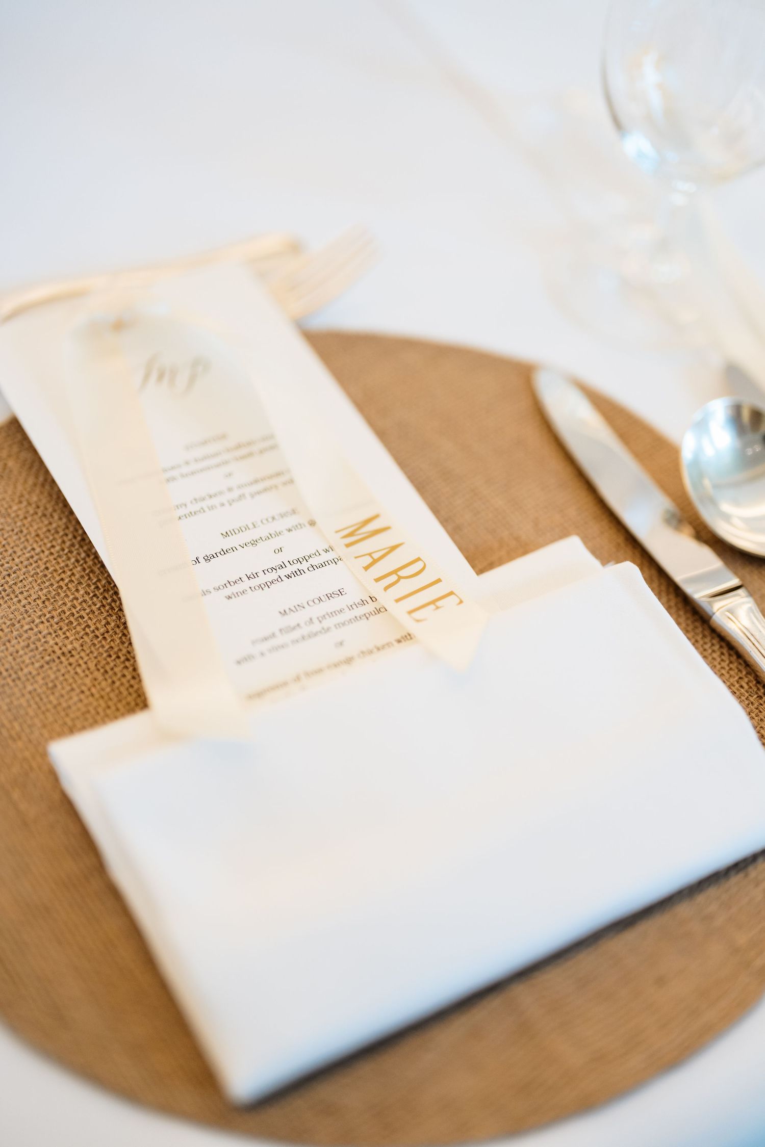 Wedding place setting features elegant white napkin and menu card on rustic bronze charger plate.
