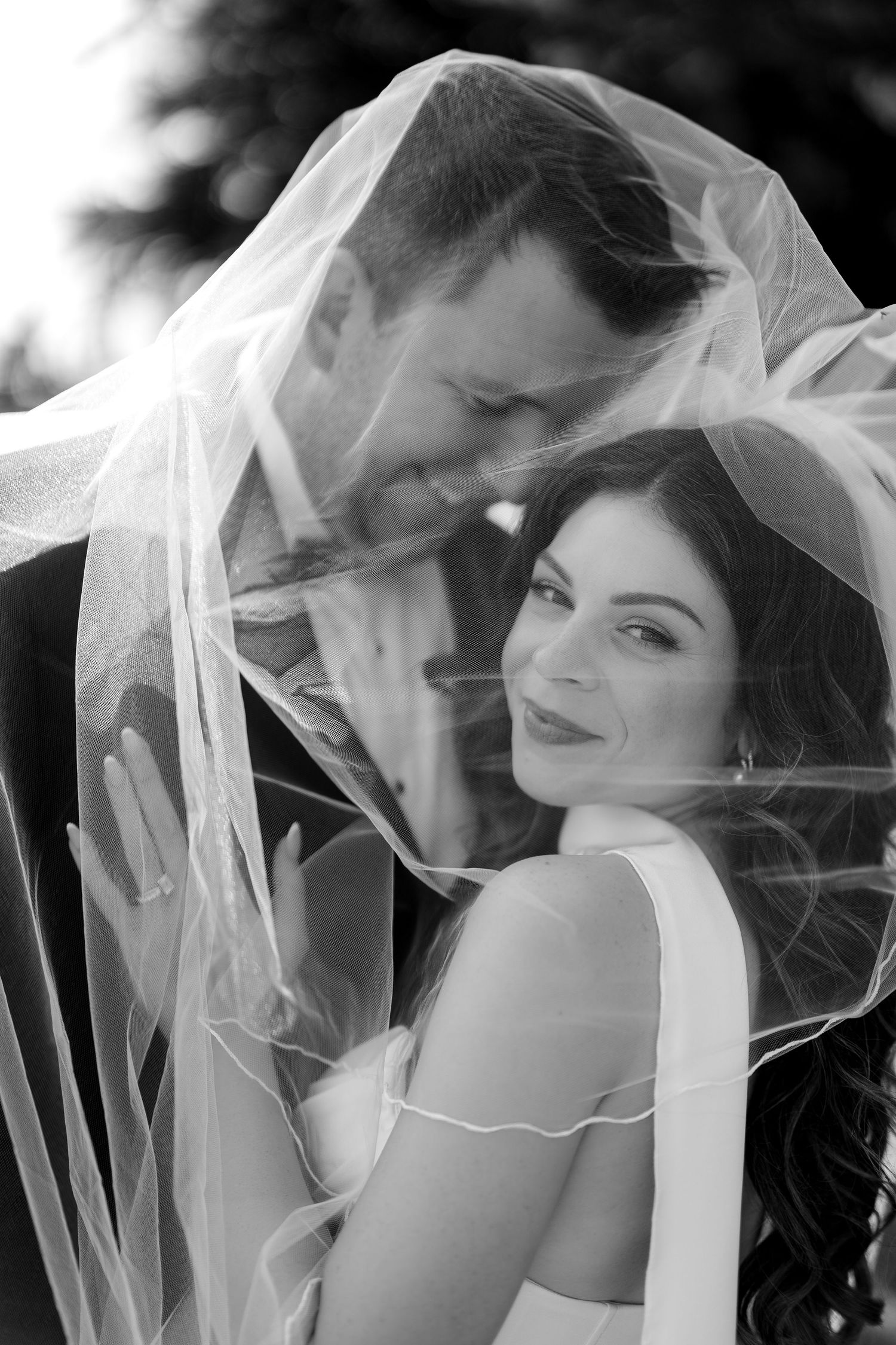 Black and white wedding portrait showing couple sharing intimate moment under flowing bridal veil.