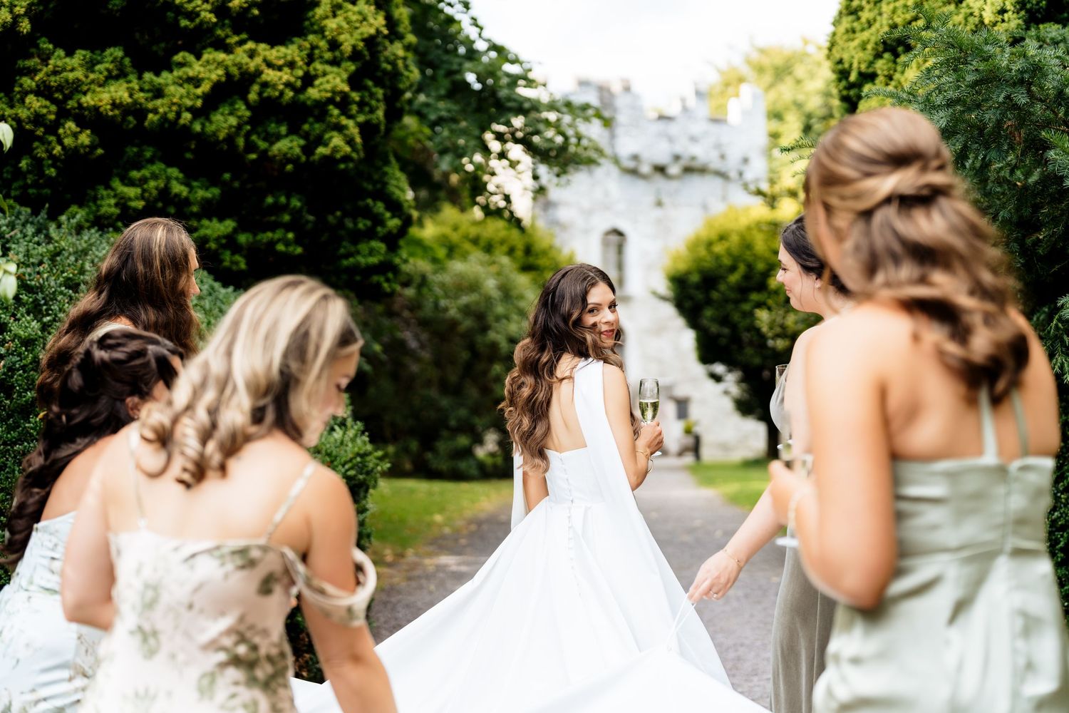 A group of bridesmaids in strapless dresses laugh and smile together during a wedding photoshoot outdoors.