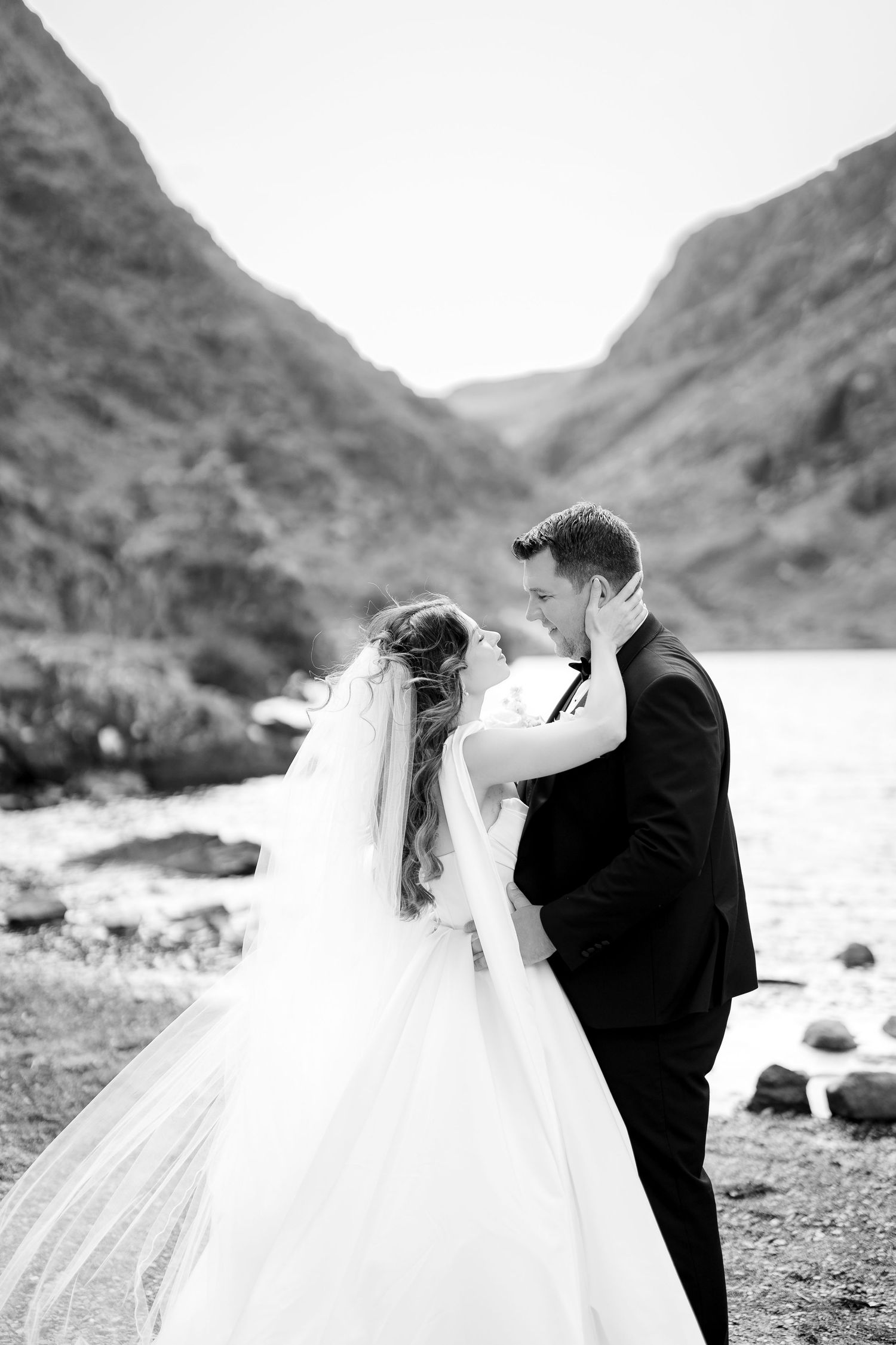 A romantic black and white photo sequence of a couple in wedding attire sharing kisses by a scenic mountainous beach.
