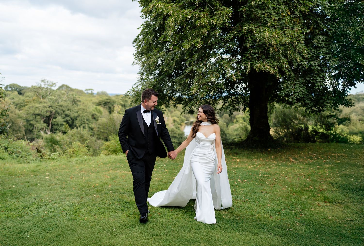 A couple walks across a lush green hillside during their outdoor wedding in nature.