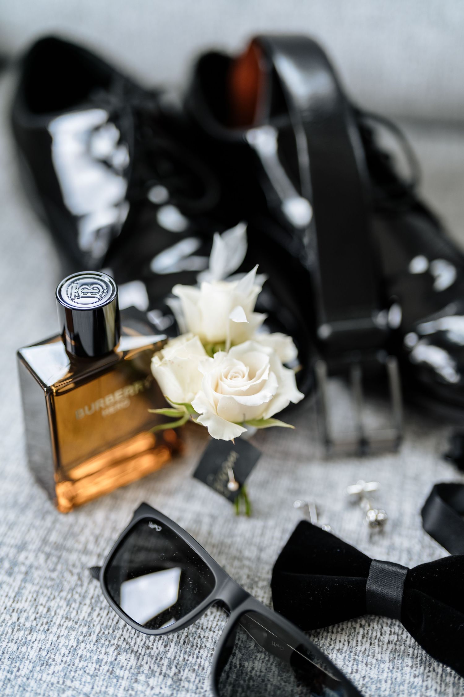 Close-up of black perfume bottles and delicate white roses on a gray textured surface.