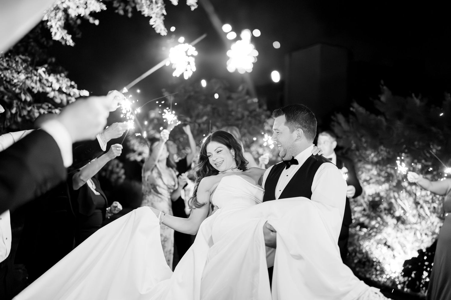 Black and white photo of a joyful dancing moment at a wedding reception with illuminated outdoor lighting creating ambiance.