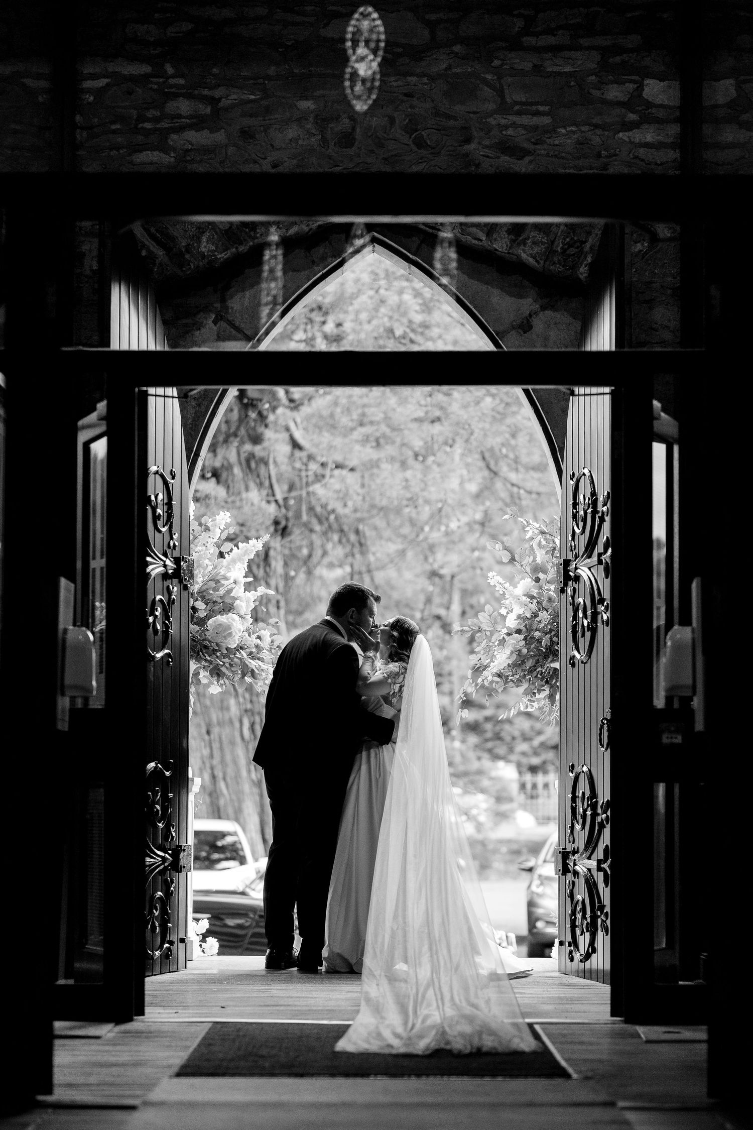 A black and white silhouetted couple share an intimate moment in a church doorway with dramatic architectural framing.