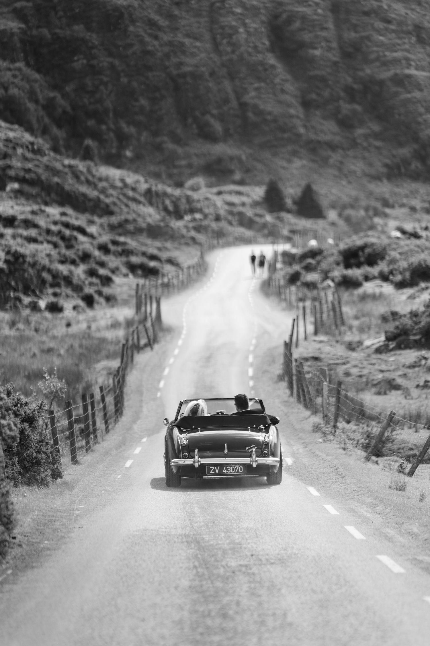 A classic convertible car on a winding mountain road through black and white photo frames.