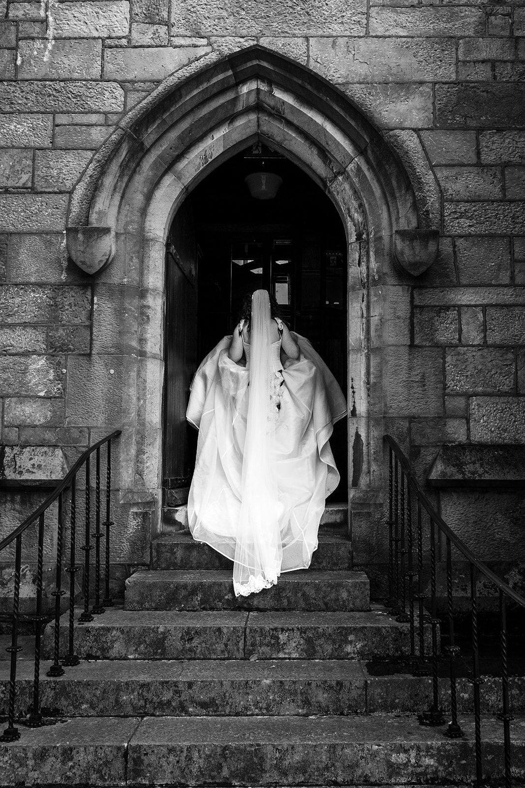 A ghostly white figure stands in a Gothic stone archway entrance of an old church, creating an eerie atmosphere.