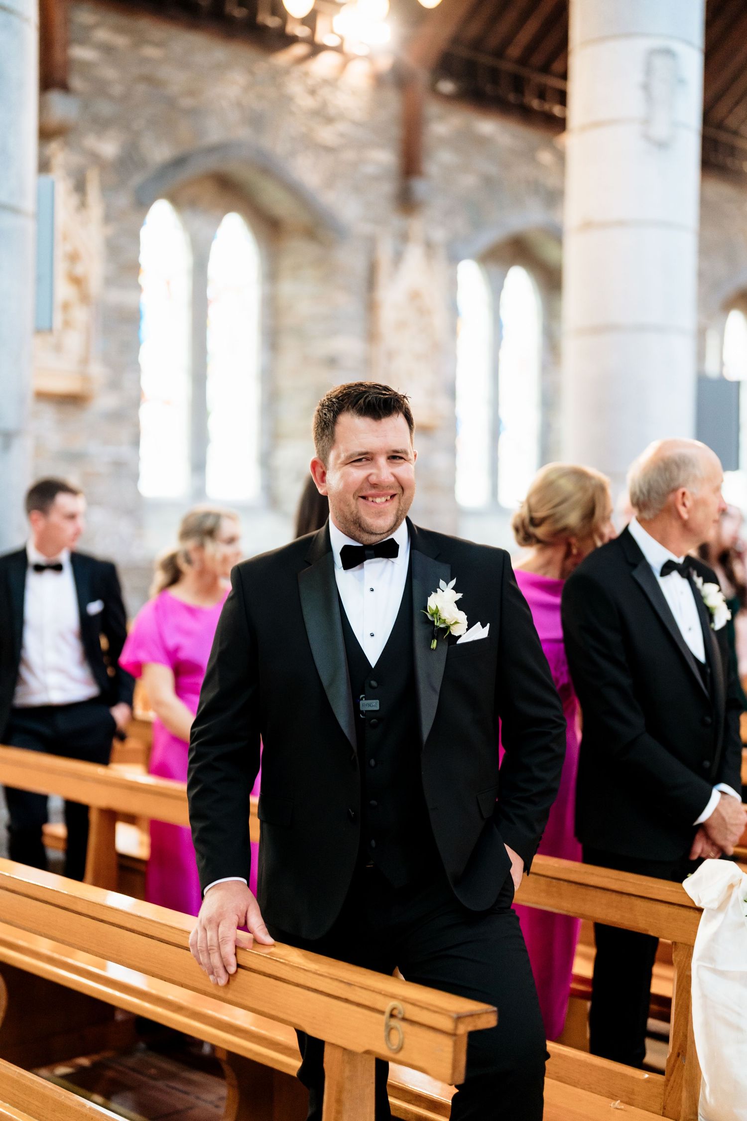 Wedding guests in formal attire sitting in wooden church pews during an elegant ceremony.
