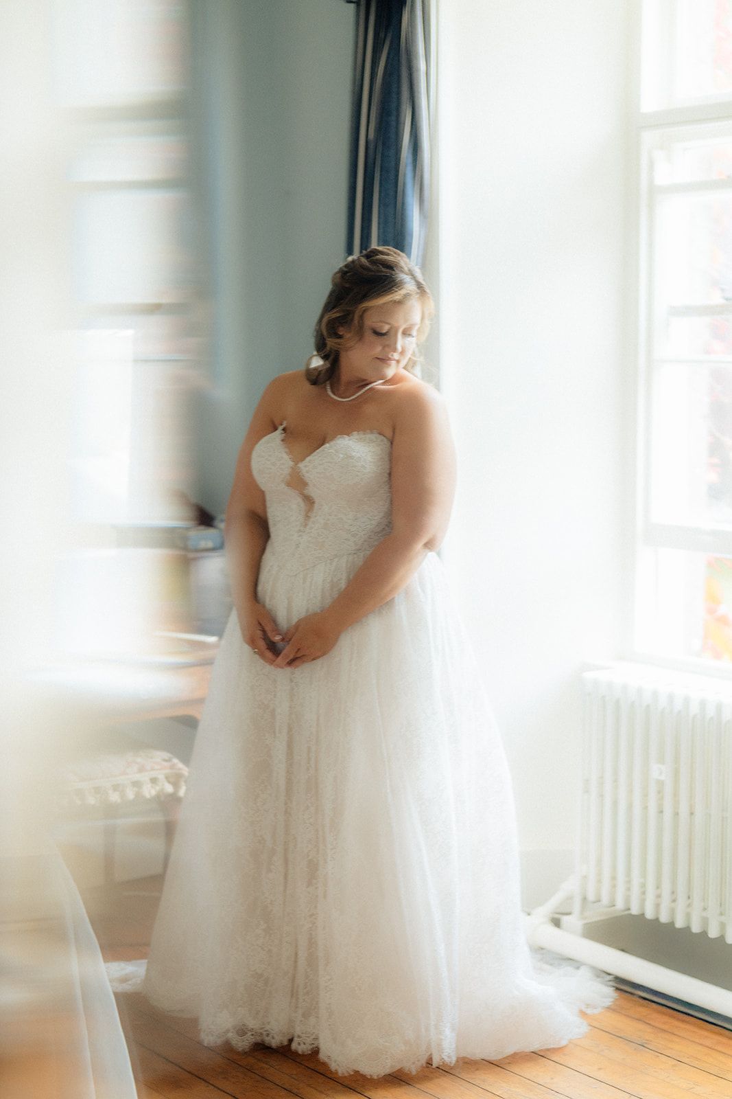 Ethereal bridal portrait series showing a flowing white lace wedding gown in a bright sunlit room with hardwood floors.