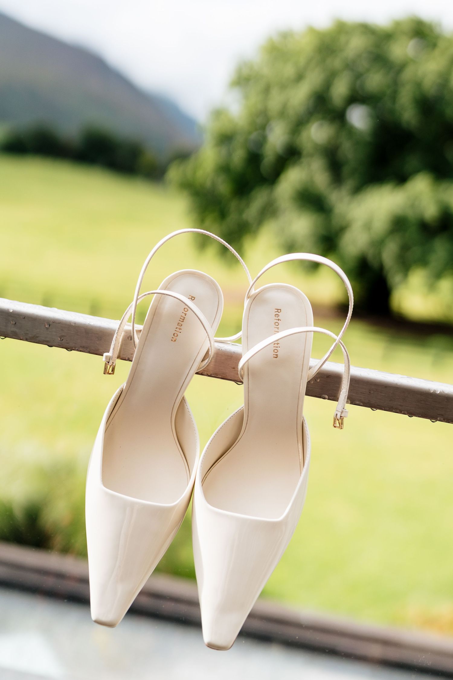 A pair of elegant white wedding shoes arranged in different positions against a blurred natural outdoor background.