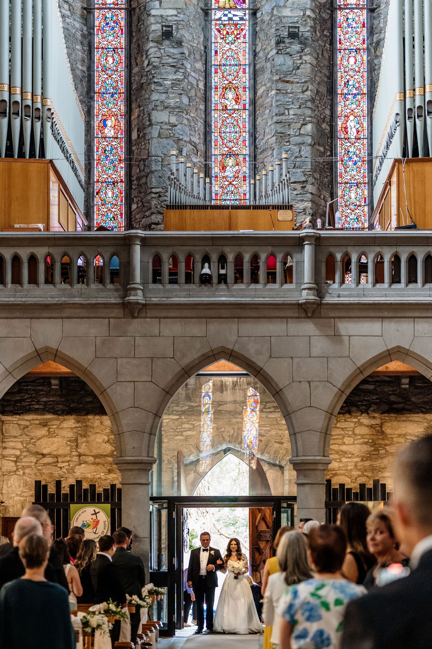 Wedding ceremony taking place in an elegant stone church with ornate stained glass windows and arched architecture.