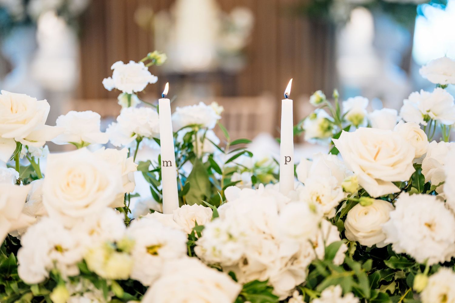 A long floral wedding centerpiece featuring white and cream roses with greenery arranged on a rustic wooden table.