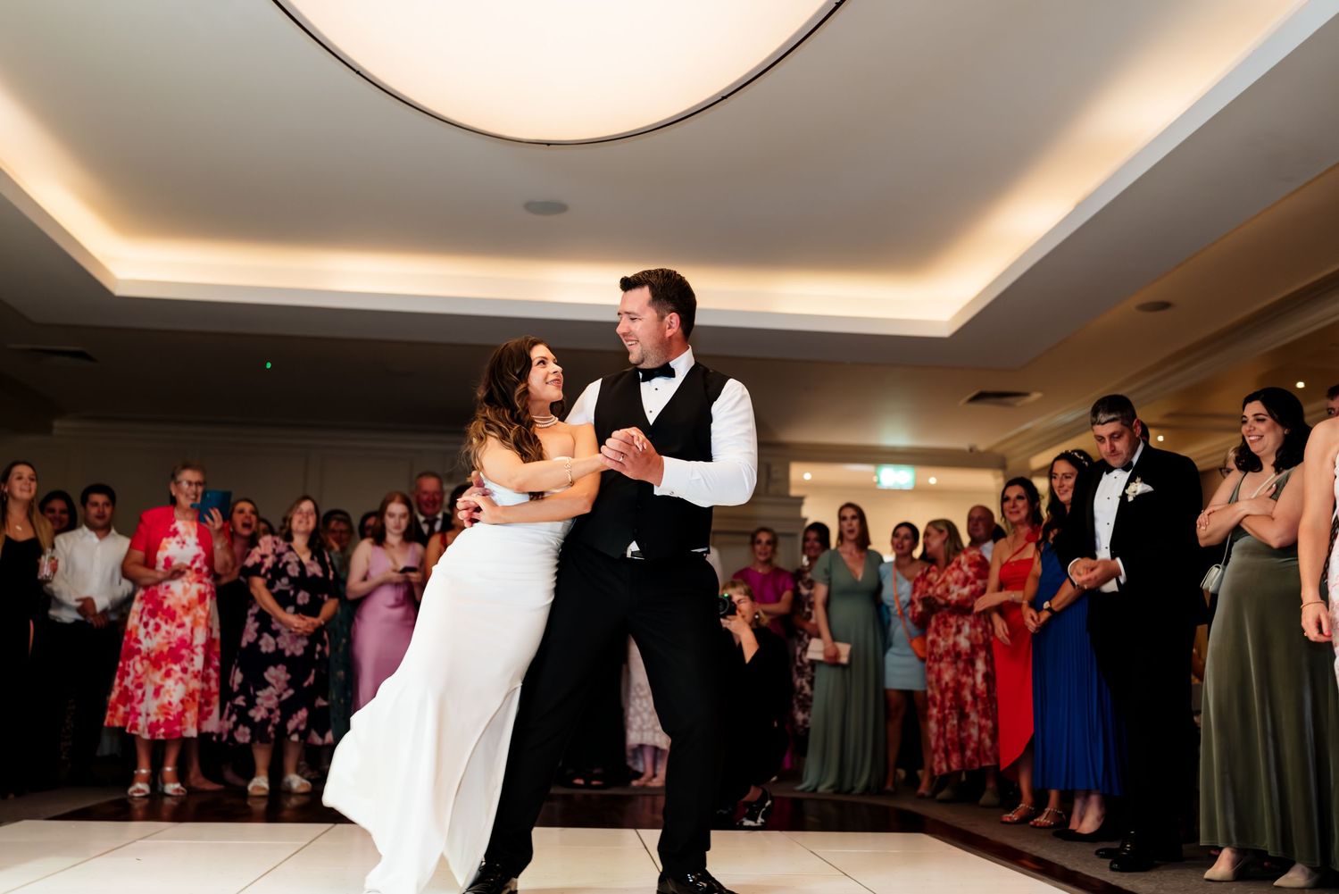 Dancing at a wedding reception as guests watch from the edges of a well-lit ballroom floor.